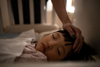 Close-up of mother hand touching sleeping girl on bed