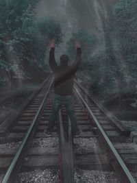 Full length rear view of man with arms raised standing on railroad track