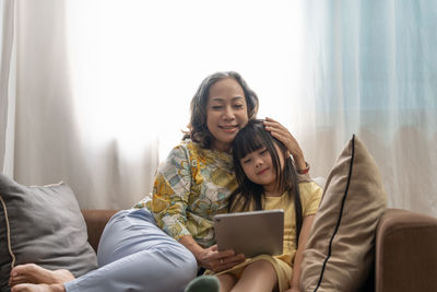 Grandmother and granddaughter using digital tablet while sitting on sofa at home