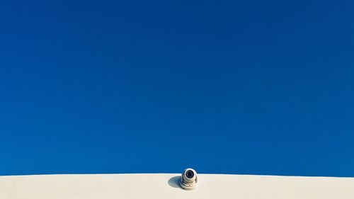 Low angle view of security camera on wall against blue sky