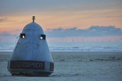 Lighthouse by sea against sky during sunset