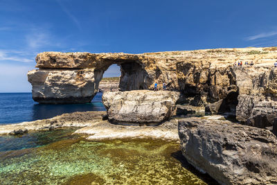 Rock formations by sea against blue sky