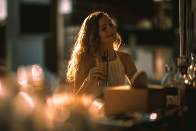 Young woman having drink at bar counter during sunset