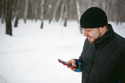 Close-up of man using phone while standing on snow covered field