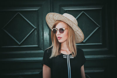Woman in sunglasses and hat standing against door