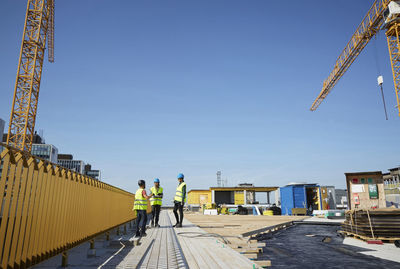 Male and female engineers discussing at construction site against blue sky