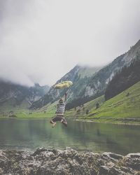 Rear view of man with umbrella jumping in lake against sky