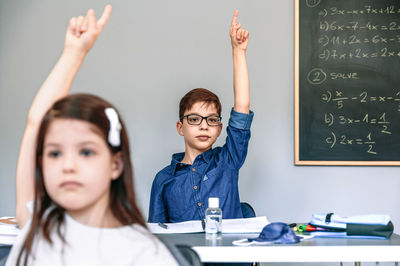 Students with mask on table raising their hands at school. selective focus on boy in background