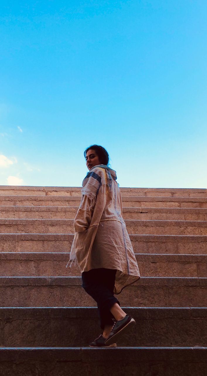 LOW ANGLE VIEW OF WOMAN STANDING AGAINST STAIRCASE