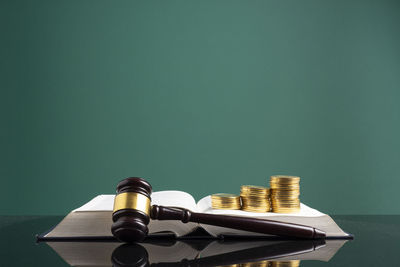 Stack of coins with gavel over open book on table against green background