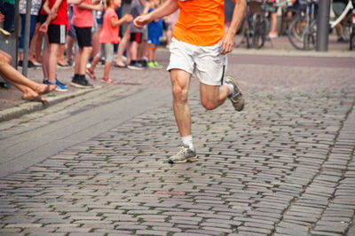 Low section of athlete running marathon on street with people cheering in background