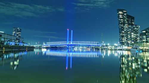 Illuminated city by river against sky at night