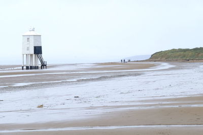 Lighthouse on beach against clear sky