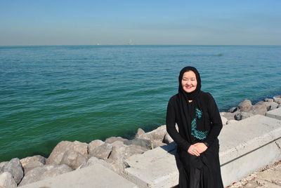 Portrait of smiling woman sitting by sea against sky