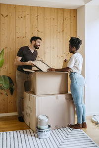 Couple unpacking boxes while standing near wooden wall at new home