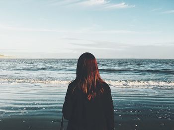 Rear view of woman standing at beach against sky