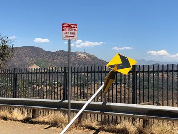 Road sign by fence against sky