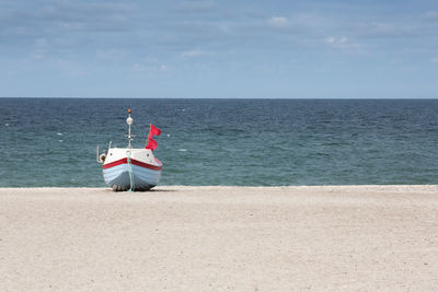 Boat moored on shore at beach against sky