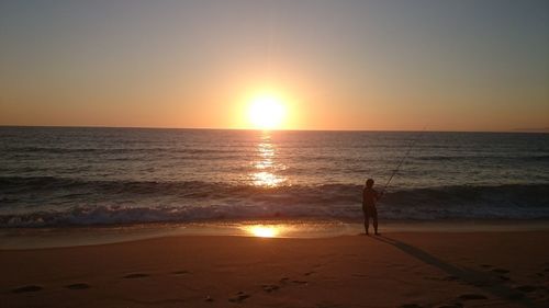Silhouette person on beach against sky during sunset