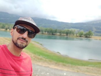 Portrait of man wearing sunglasses and cap against lake