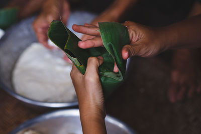 High angle view of woman wrapping rice cakes in banana leaf cone