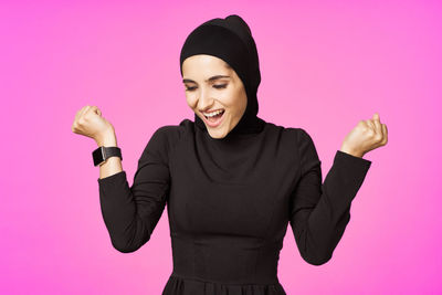 Smiling young woman standing against pink background