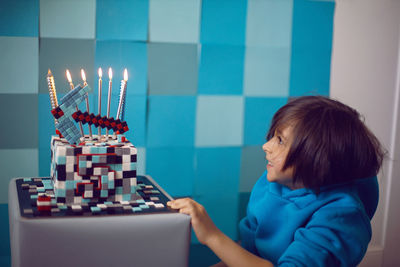 Boy child in blue clothes and a cap is sitting on a gray square celebrating his birthday. 