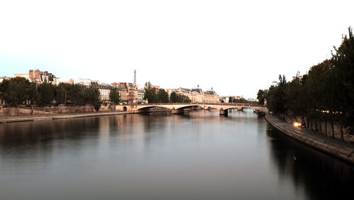 Bridge over river by buildings against clear sky