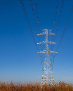 Electric pole and electric cable on the field in the countryside with blue sky.