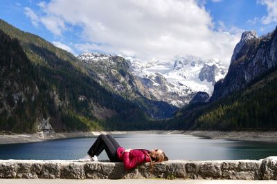 Girl relaxing in front of scenic view of lake and mountains against sky