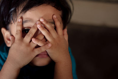 Close-up of boy covering face with hands