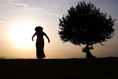 Silhouette woman standing on field against sky during sunset