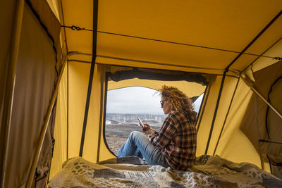 Side view of mature woman using smart phone while sitting in tent at beach