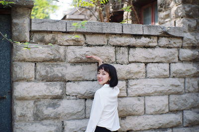 Portrait of smiling young woman standing against stone wall