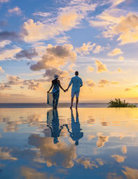 Silhouette woman standing at beach against sky during sunset