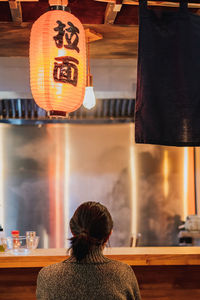 Rear view of woman with illuminated lanterns hanging on table