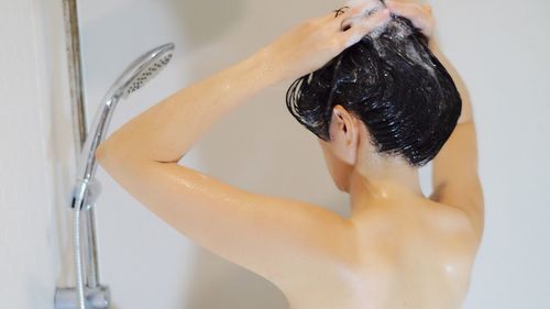 Rear view of shirtless woman taking bath in bathroom