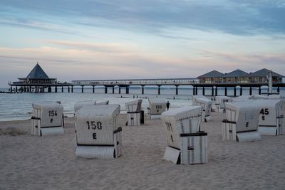 Hooded chairs on beach against sky during sunset