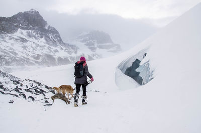 Woman with dog walking on snow covered mountains