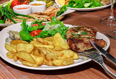 Table with various meat and vegetable dishes and fried potatoes