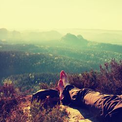 Long tired male legs in hiking trousers take a rest on peak of rock above valley.