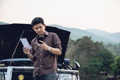 Man using smart phone while standing by vehicle