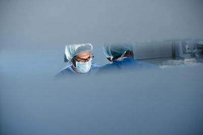 Male surgeons seen from glass while performing operation in hospital