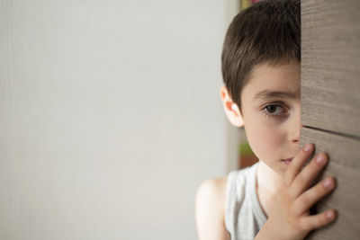 Boy looking away while peeking by door