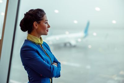 Side view of young woman looking away while standing against sky