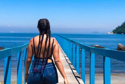Rear view of woman with braided hair standing on footbridge against sea