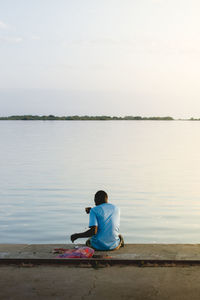 Rear view of man sitting by lake