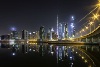 Illuminated buildings by river against sky at night