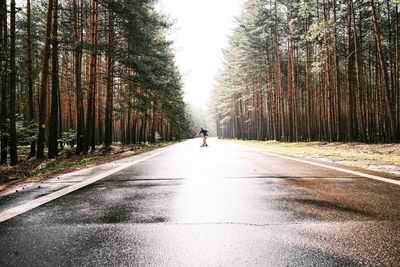 Man on road amidst trees against sky
