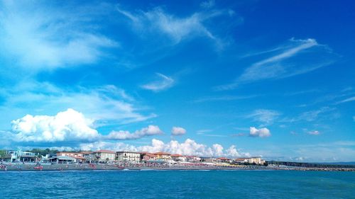 Buildings by sea against cloudy sky